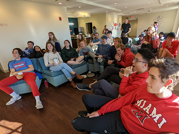 a large group of students watching tv together in their dorm common area