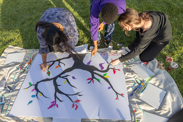 Three students working on an art project on the ground outside
