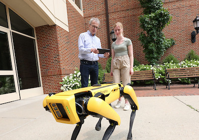 a student and faculty member observing a robot dog.