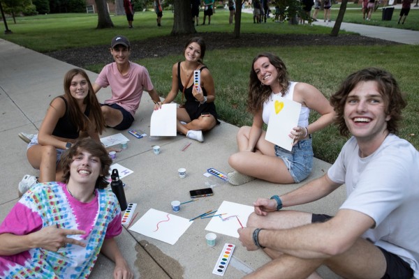 Group of about 7 students doing some artwork on the ground.