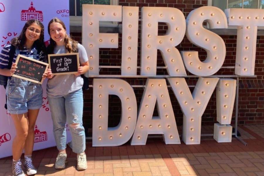 Two students holding up a sign that says First day of 13th grade in front of light-up marquise letters that read first day.