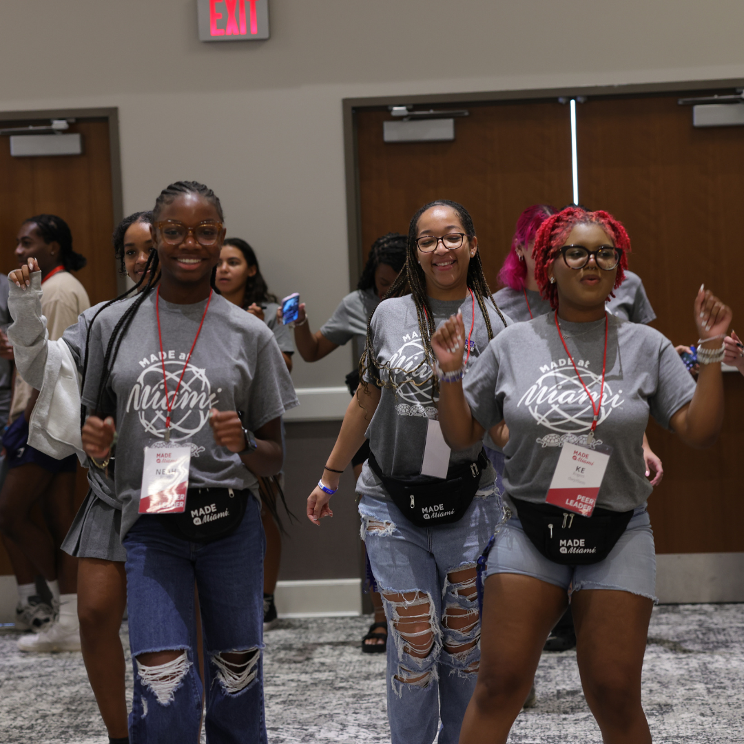 A group of students in gray MADE at Miami shirts and peer leader nametags dancing in a line. 