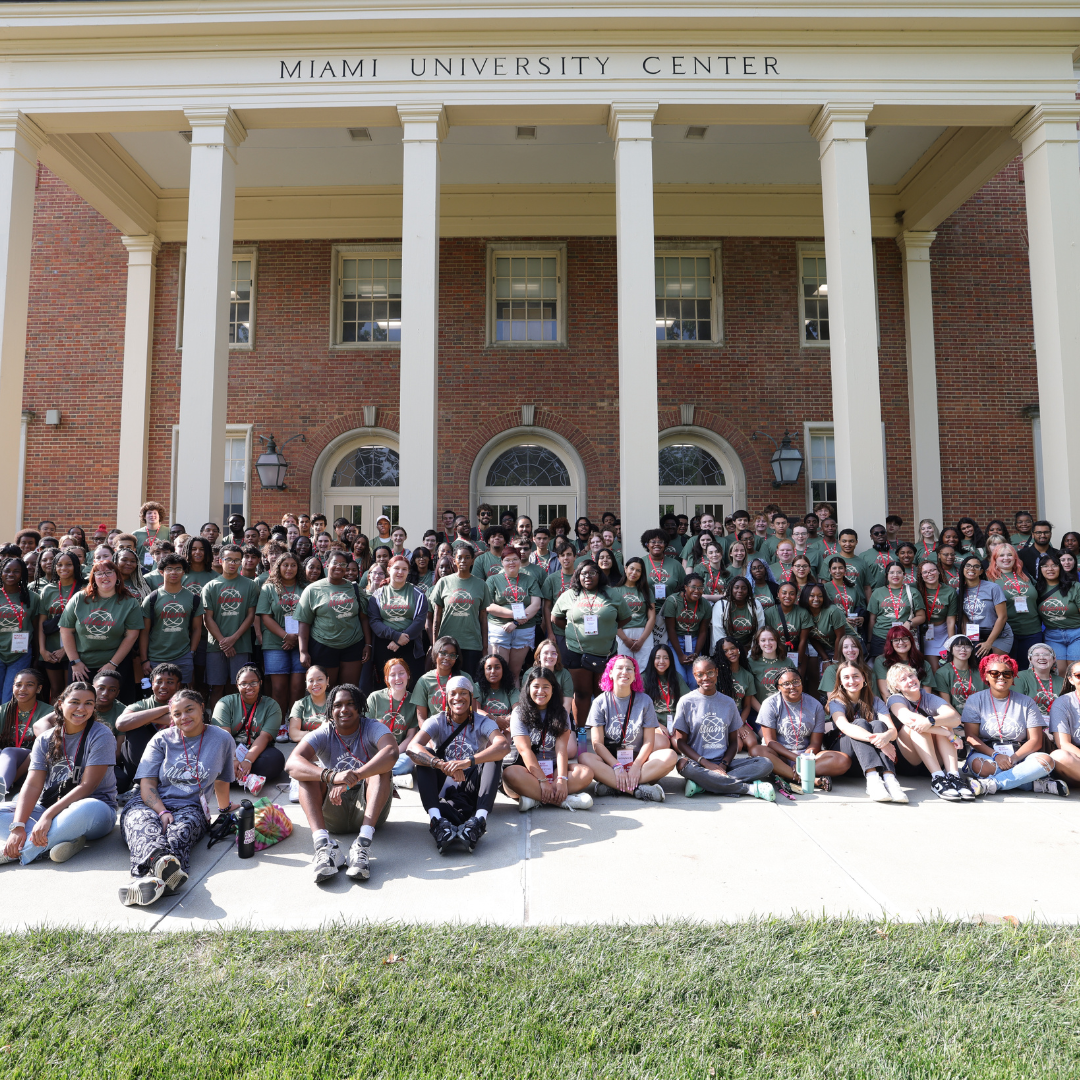 Huge group of about 100 students wearing green or gray MADE at miami shirts, posing in front of the Shriver Center.