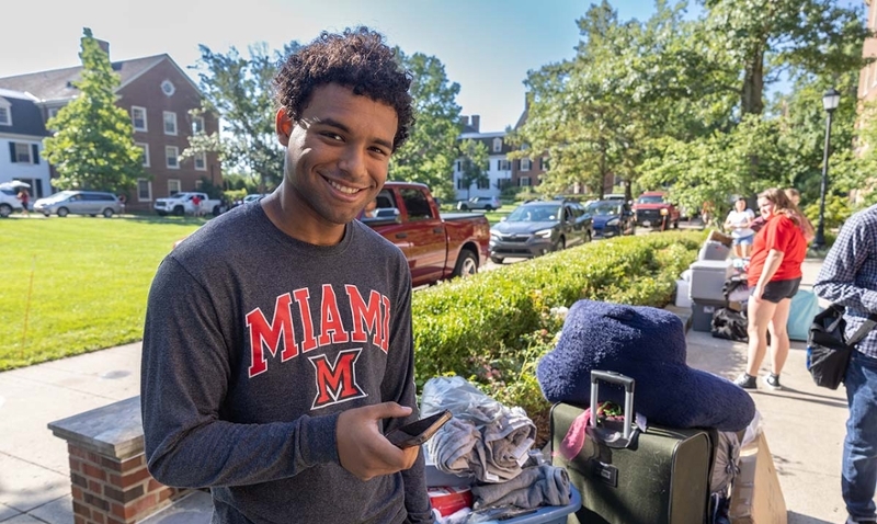 A student poses for a photo while holding their phone