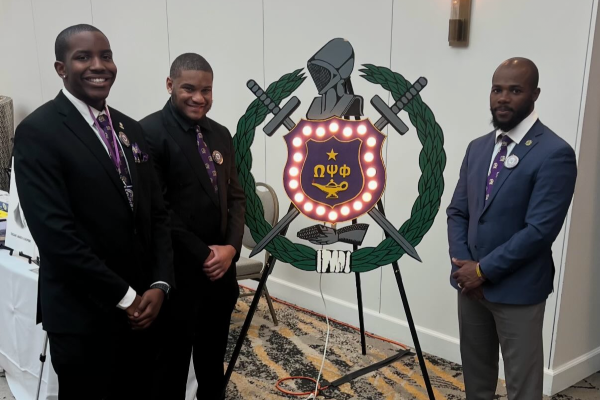 Three men in suits, standing around a shield from Omega Psi Phi Fraternity, Inc.