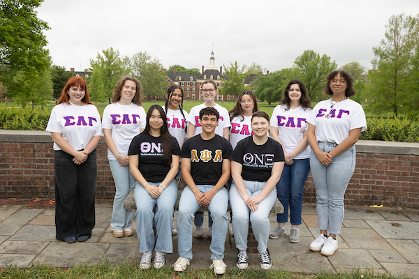 10 students in greek letter shirts, posing in front of central quad.