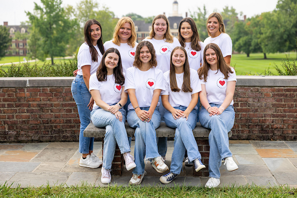 9 female students wearing Panhellenic related shirts and standing in front of south quad.