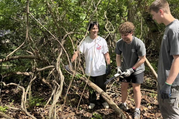 Three students in the woods with various shovels and tools.