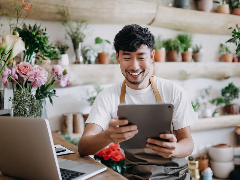 A student professional smiles while using a tablet in a floral design studio.