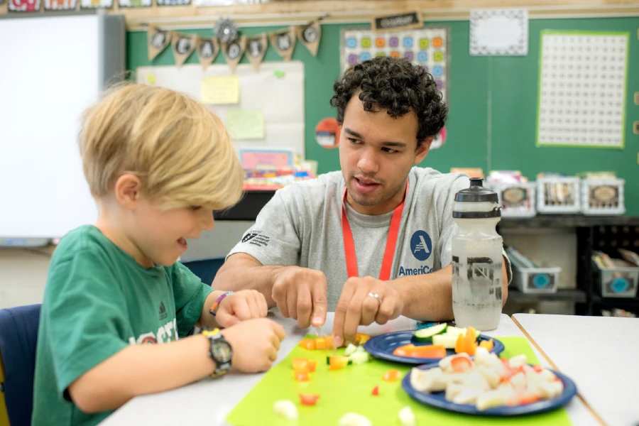 Student wearing an AmeriCorps program shirt working in classroom with young child.