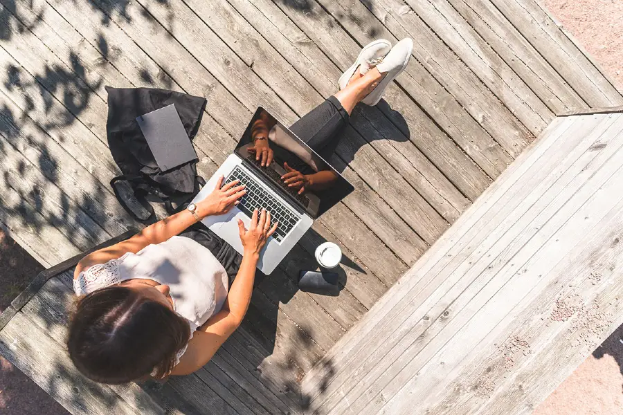 An aerial view of a student sitting on deck with laptop and bag.