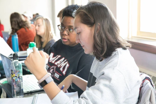 Female students working in classroom and looking at laptop.