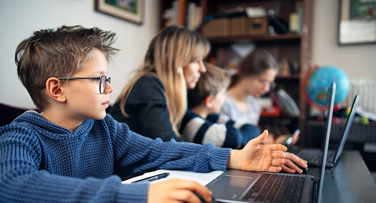 Young students working with laptop at a desk with other students.