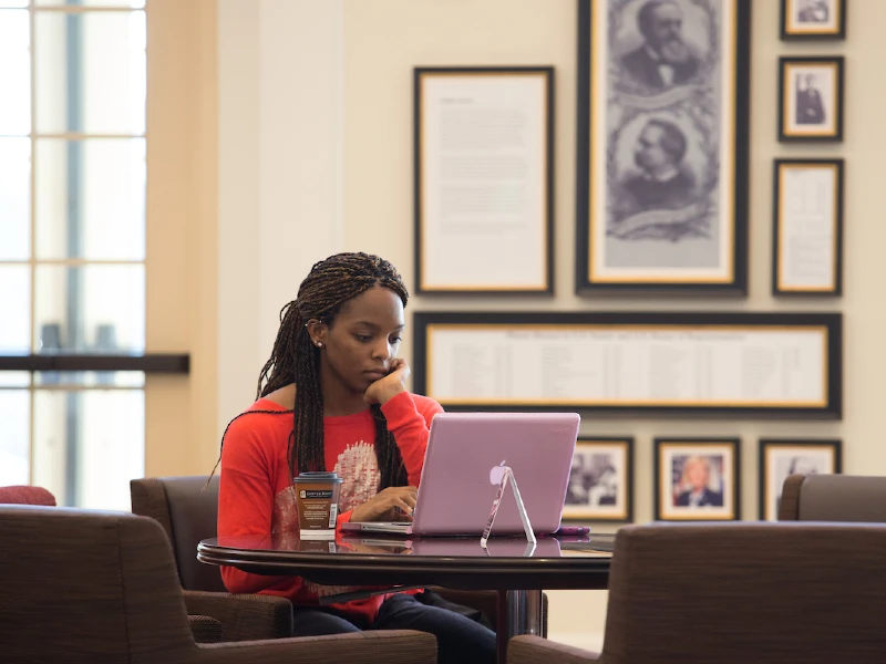 A student sitting in chair in lobby with laptop computer.