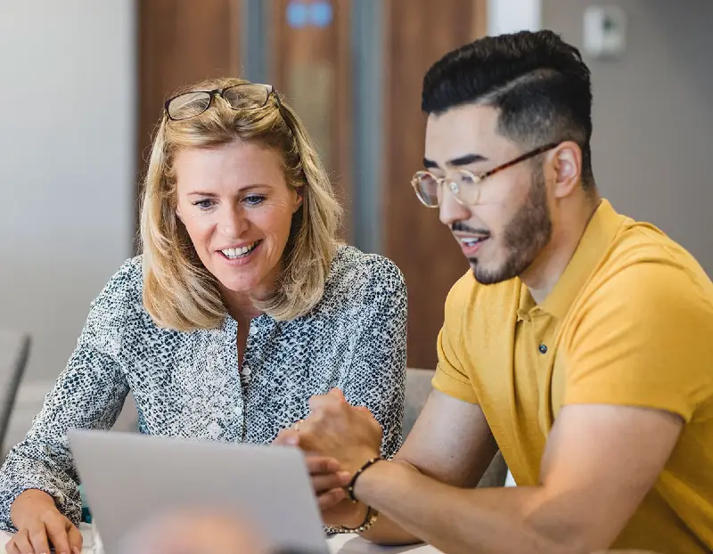 Woman working with male student on laptop computer.