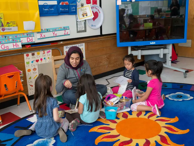 Teacher in classroom with young students sitting on rug. 