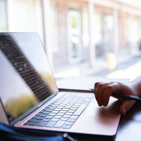 A laptop in a coffee shop with someone holding a pencil