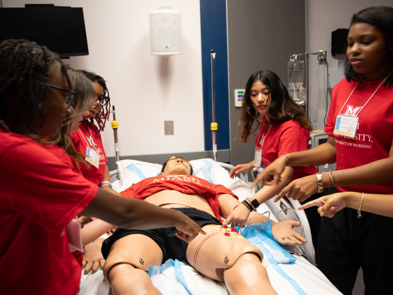 Students working on a nursing simulation where the leg is bleeding.