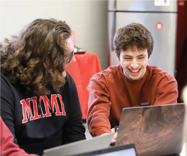 2 students working on a laptop smiling. 
