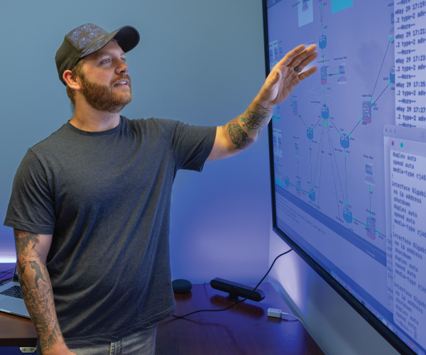 A veteran student pointing at a large screen on the wall with code.