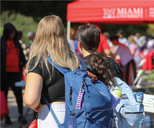 2 students walking outside with their backpacks. 
