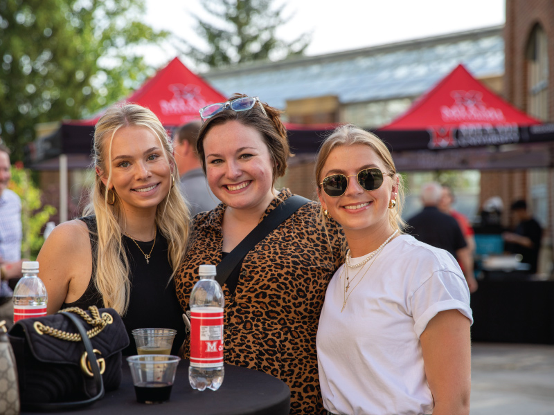 Three women smiling at the camera during a happy hour event at the Conservatory on the Miami Hamilton campus