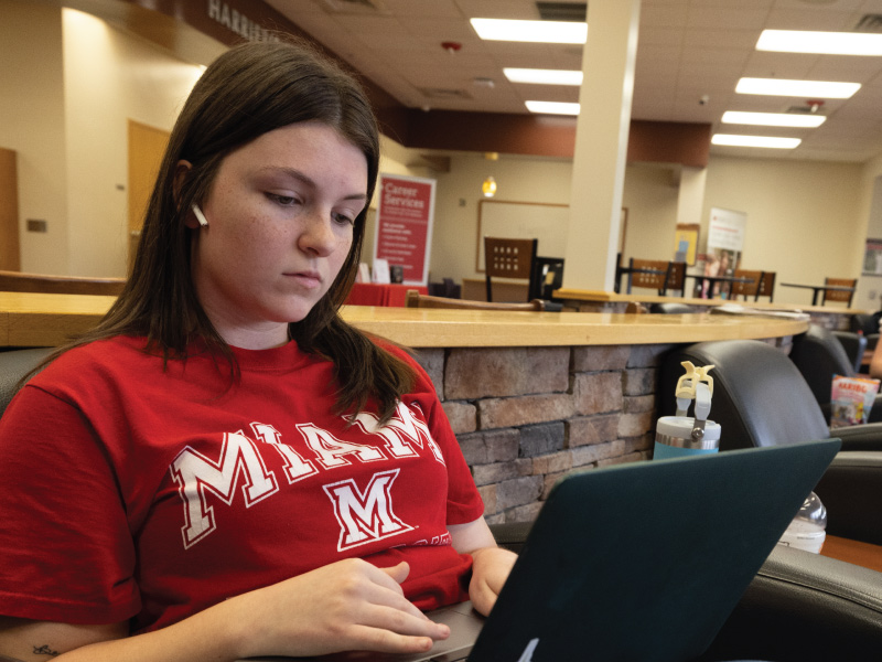 Student sitting in Harrier's Nest on the Hamilton Campus working on her laptop.