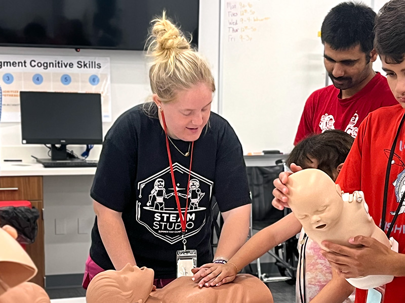A STEAM counselor helping campers learn CPR