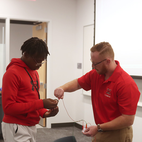A STEAM leader helping a teen connect a circuit