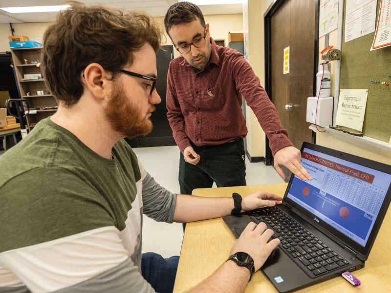 Professor helping a student on his laptop during class. 