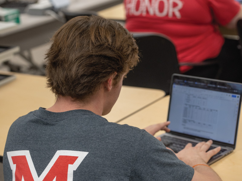 Student in class typing notes on his laptop
