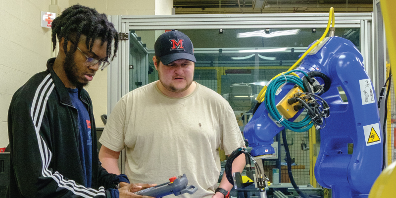 2 students using a remote control to work a robot.