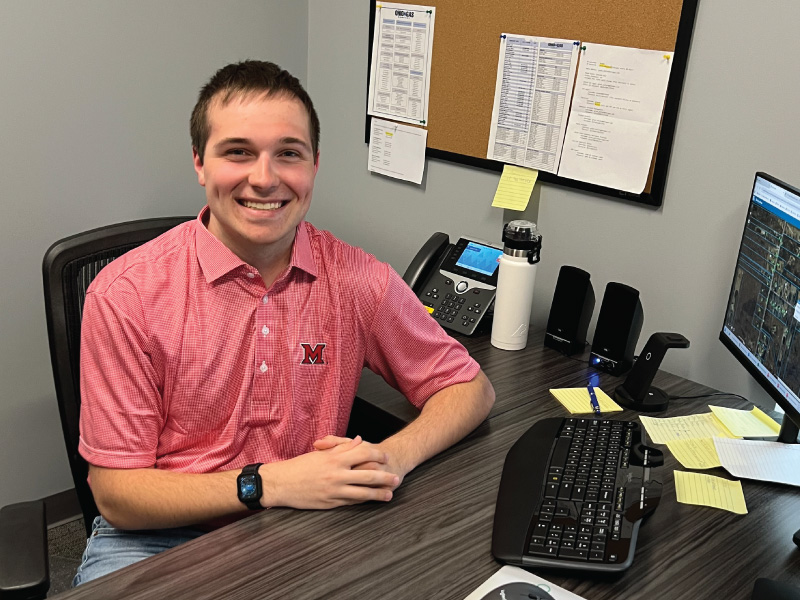 Grant Keller at his desk at work wearing a Miami polo