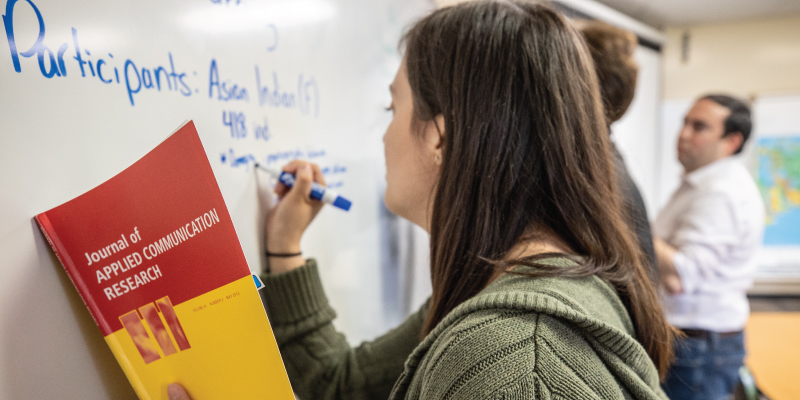 A student writing on the white board reading from her communication book. 