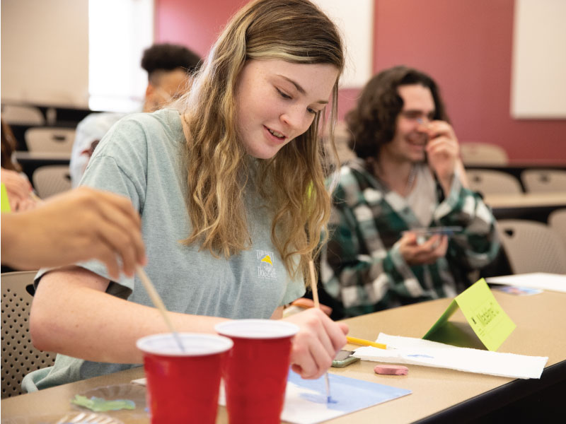 Student using blue paint on a white piece of paper. 