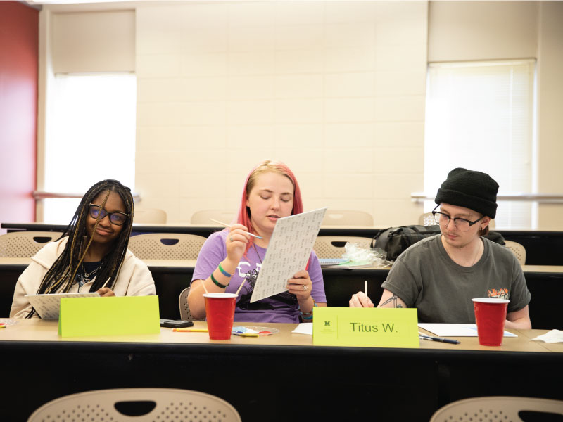 3 students discussing while painting.