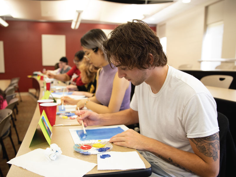 A student painting his paper with blue paint. 