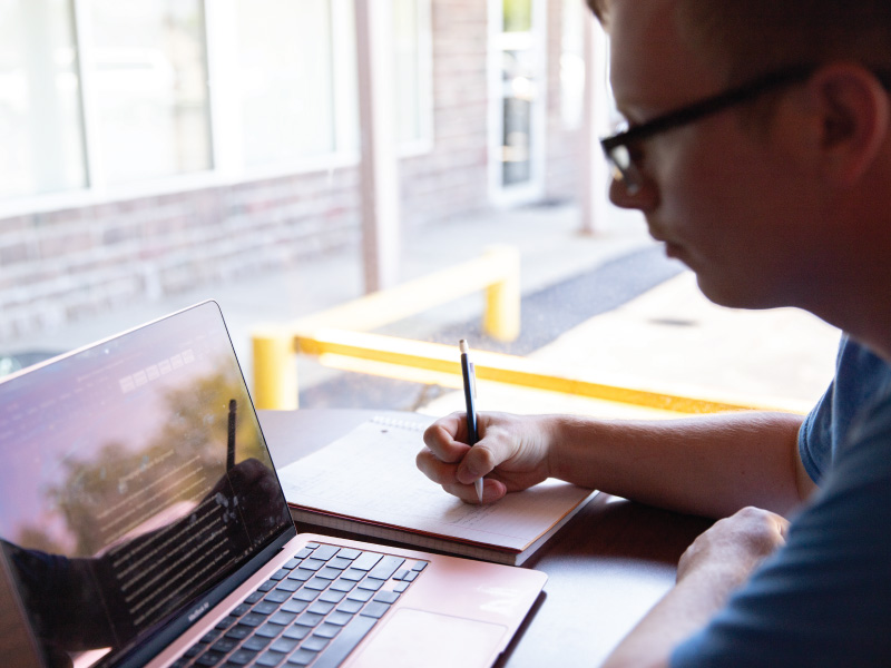 Ethan Sander, Psychology Club student working on his laptop and taking notes in a notebook.