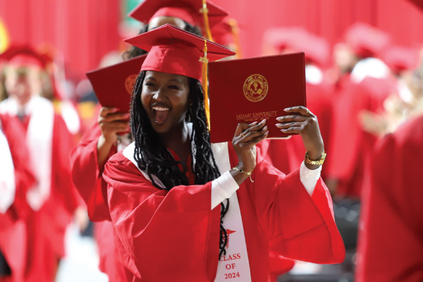 CLAAS graduate holding up her diploma in her cap and gown at commencement.