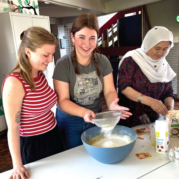 2 students sifting flower into a bowl at the Refugee Center Hëllef um Terrain.
