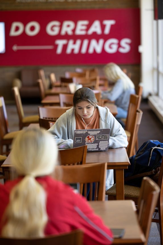 Students work on their laptops independently with a sign in the background that reads "Do Great Things."