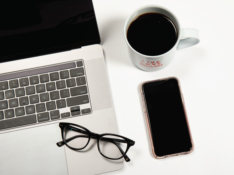 Laptop, coffee cup, glasses and cell phone on a table.