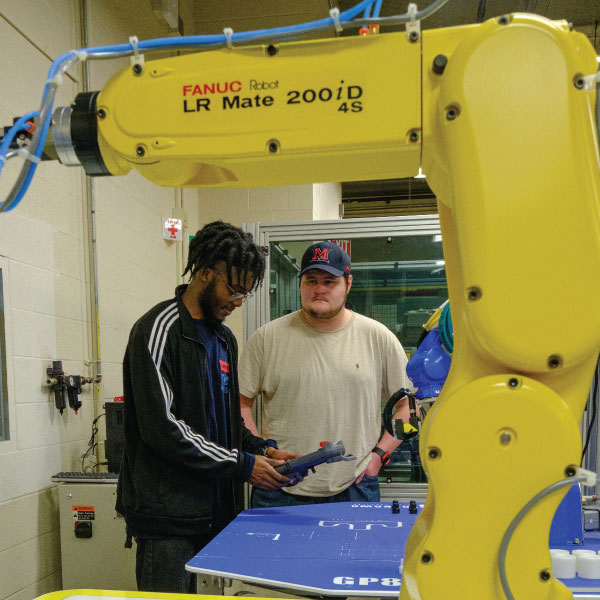 Two students working with a very large yellow robotic arm